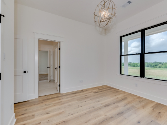 Bedroom with light wood flooring and windows with black trim.
