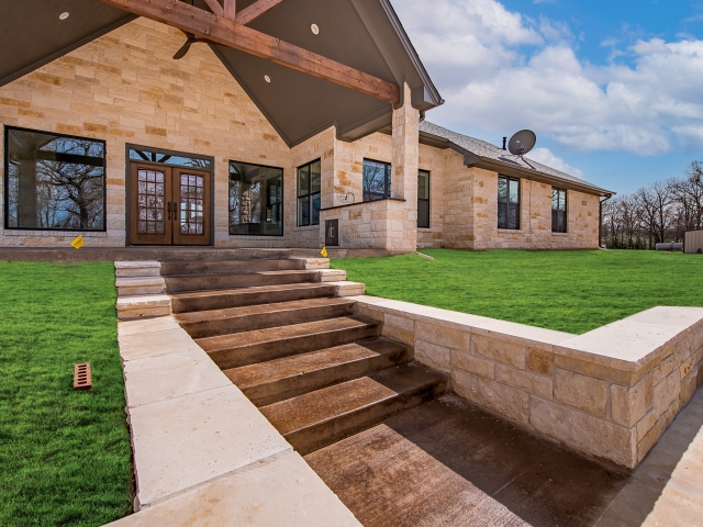 Stone accented backyard of the Taylor Custom Home with a lush lawn.