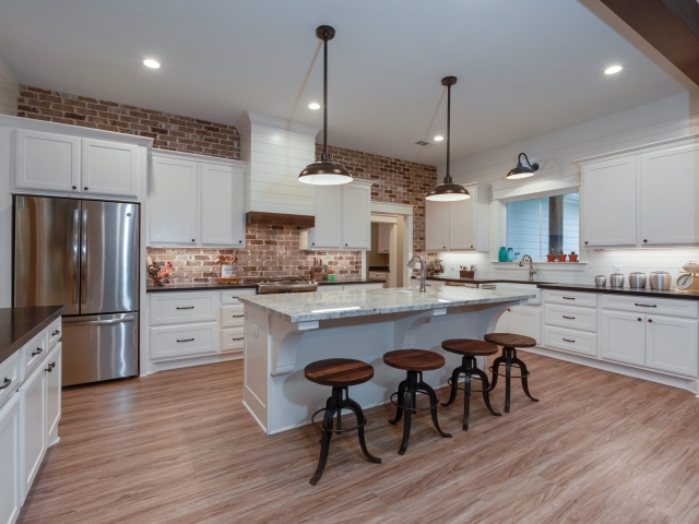 The Moore Project&#039;s kitchen by LaFollette Custom Homes features white cabinets and a brick backsplash.