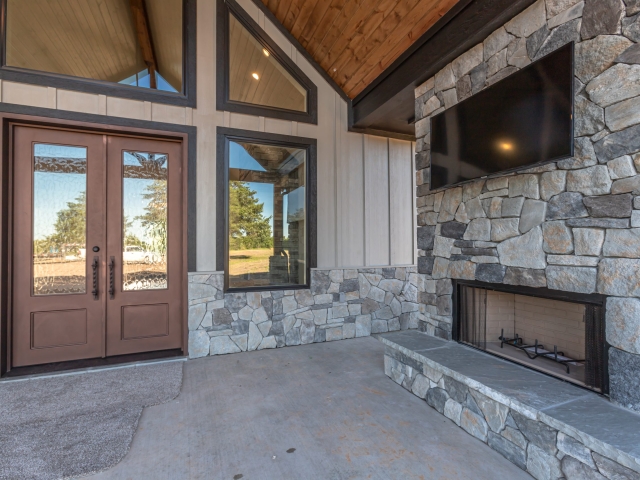 Back porch of the Millican Custom Home with black trim windows, fireplace, and grey stone walls.