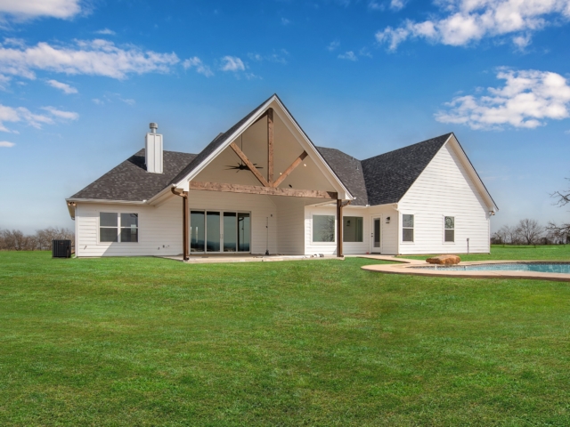 The Garrett Custom Home with white exterior and wood detailing on a green lawn.