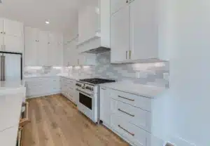 Modern kitchen with white cabinets and appliances, light brown wooden floors, and soft under-cabinet lighting for a warm, inviting ambiance.