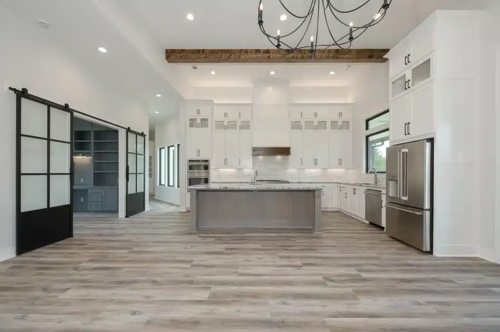 Current image: Modern kitchen with white cabinets, gray island, stainless steel appliances, and sliding glass barn doors.